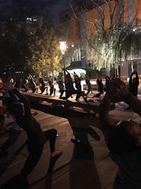 a group of people doing yoga on a park bench at night