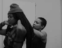 a black and white photo of a woman putting on a hat